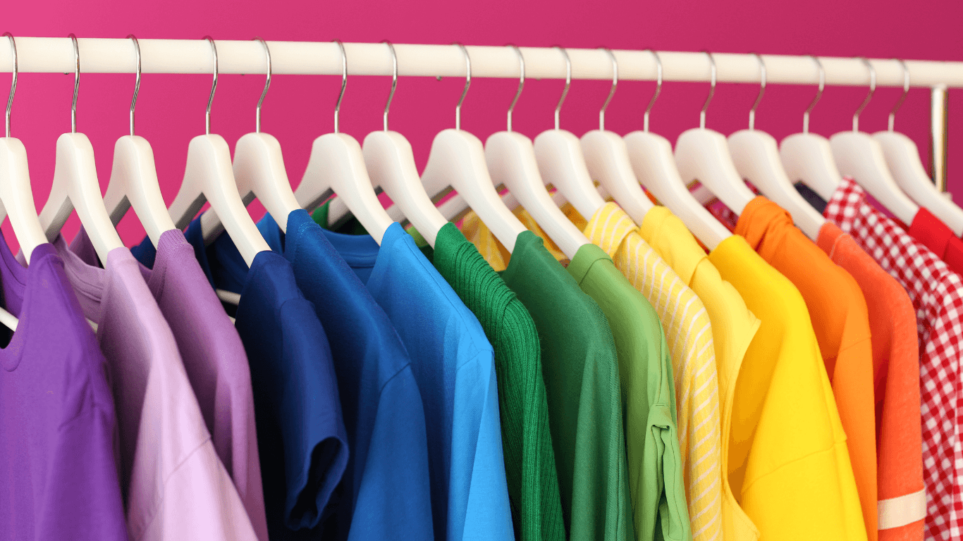 Multi colored clothes hanging on plastic hangers behind pink wall