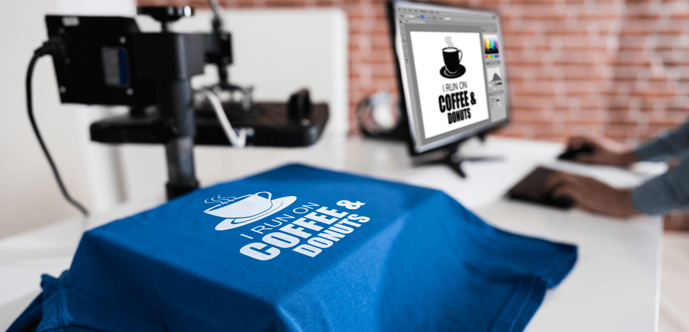 Man using computer designing logos for merch using Photoshop beside blue T-shirt using heat transfer